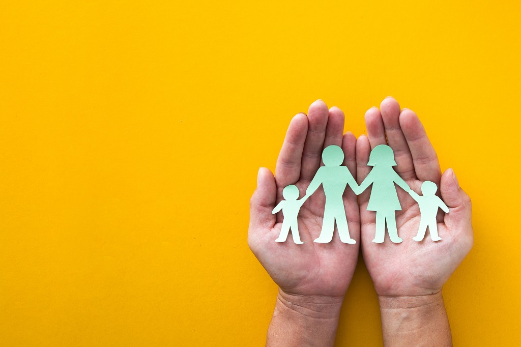 Imagine of two hands, palms raised holding paper cutouts of a family holding hands